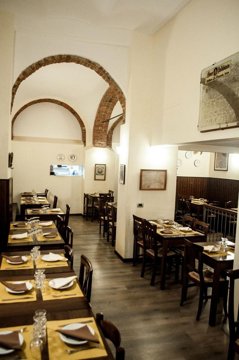 La sala lunga con archi in mattoni e tavoli apparecchiati con tovagliette color senape